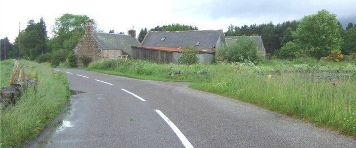 A rural road with stone buildings and lush greenery.