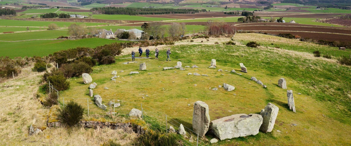 A stone circle in a grassy field with rolling hills in the background.
