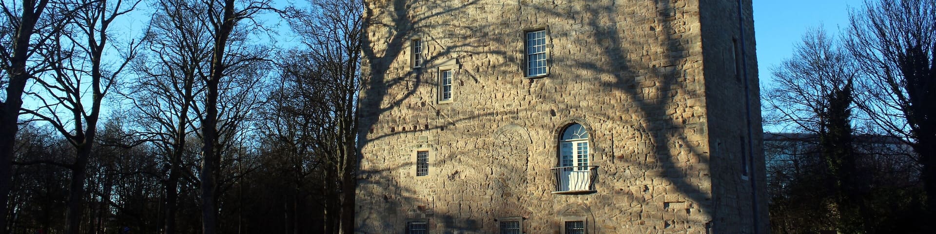 A historic stone castle with battlements, surrounded by a park with leafless trees.