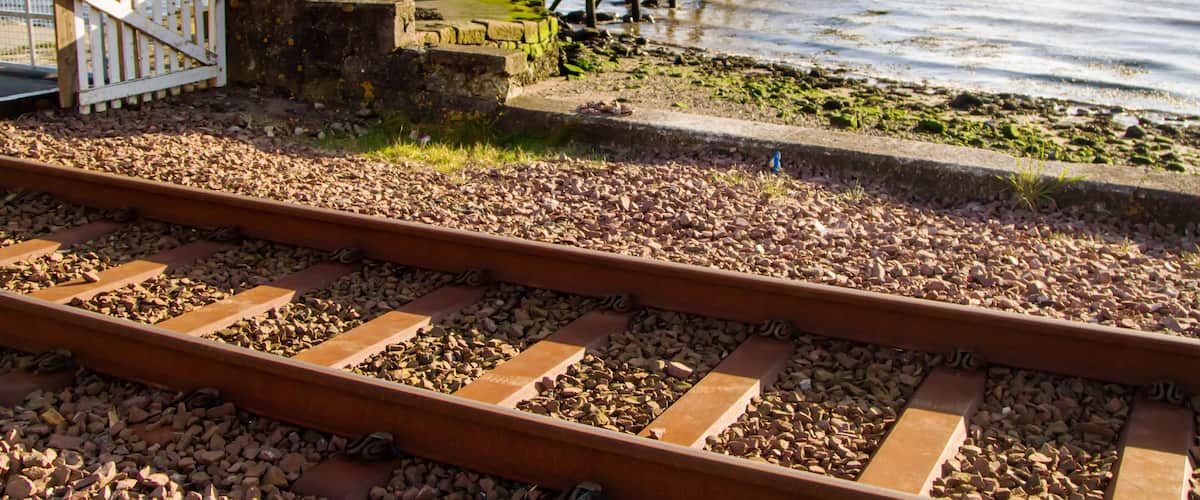A coastal railway track, a wooden pier, and a flag on a post.