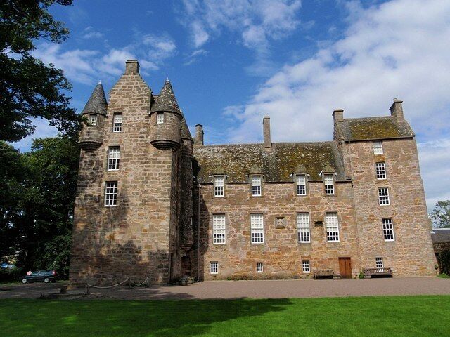 A large stone castle with multiple towers and a well-maintained lawn in front.