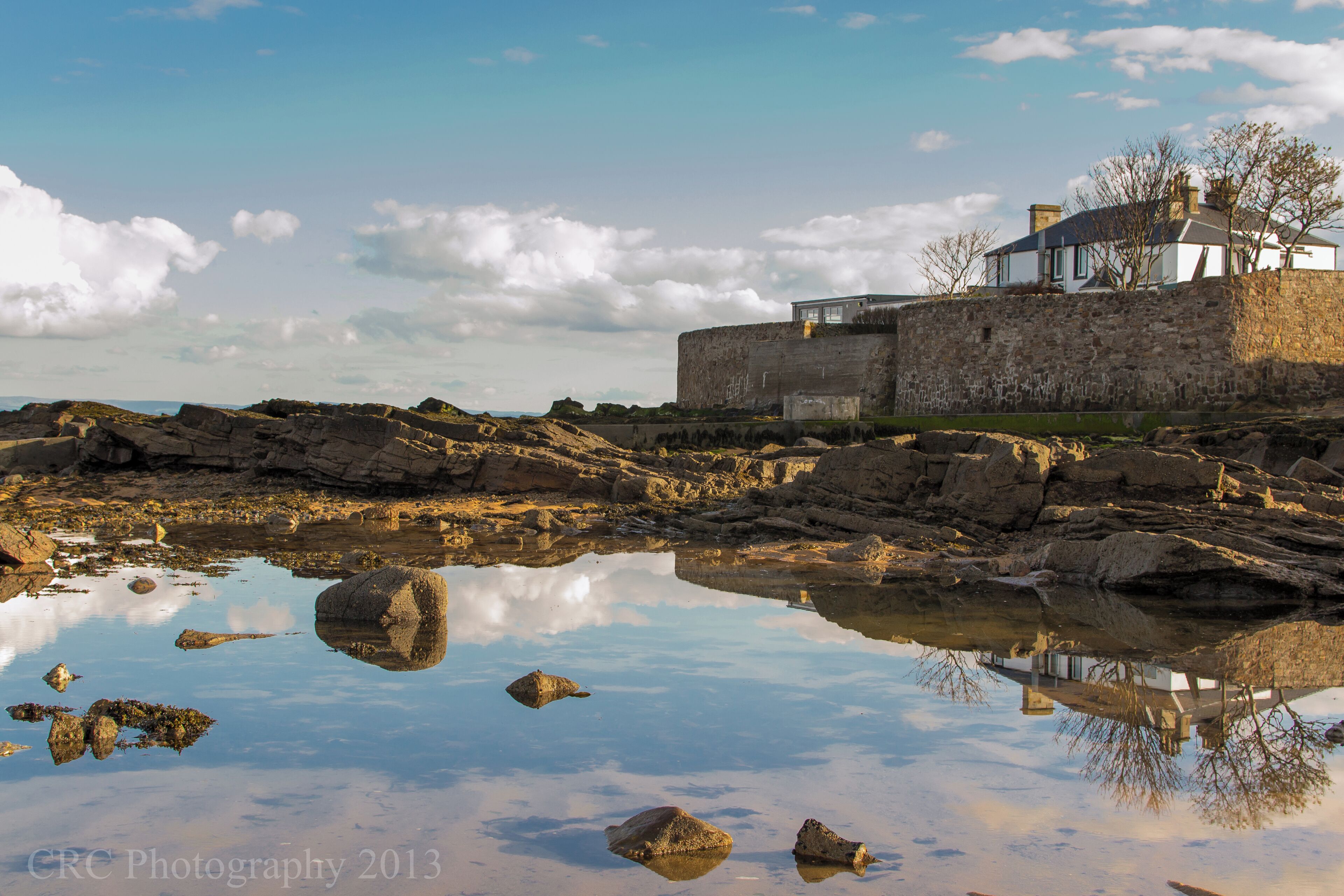 A coastal house with a stone wall and a rocky shoreline.