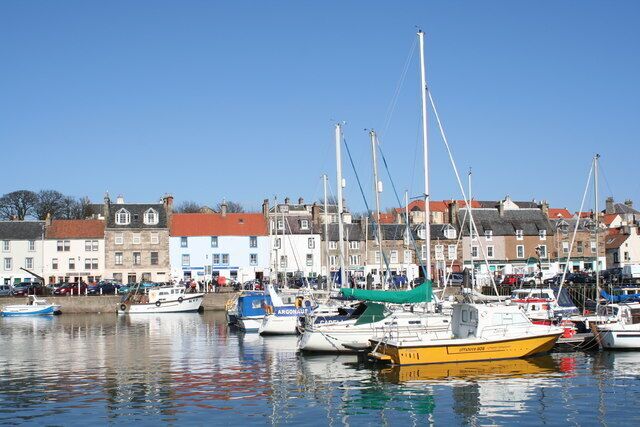 A harbor with boats docked, buildings in the background, and a clear blue sky.