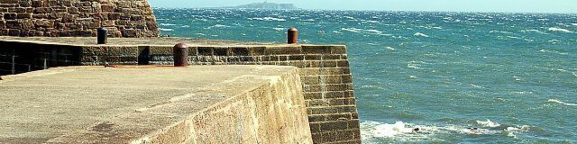 Un muelle de piedra que se adentra en el mar, con olas rompiendo contra él.
