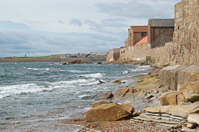 A rocky coastline with a historic stone building and waves crashing against the shore.