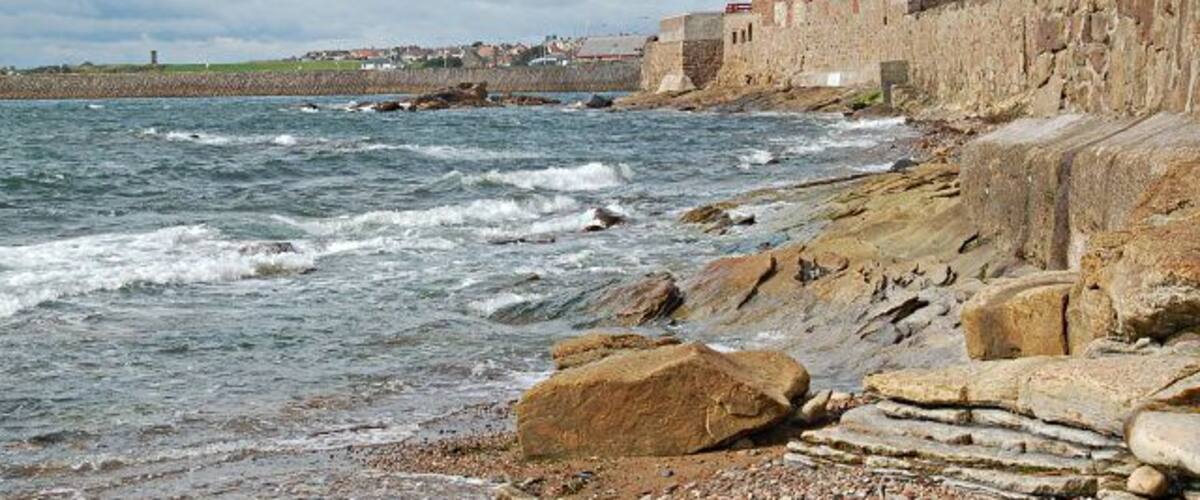 A rocky coastline with a historic stone building and waves crashing against the shore.