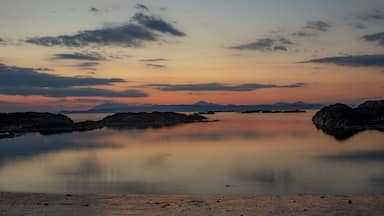 A calm lake at sunset with mountains in the background.