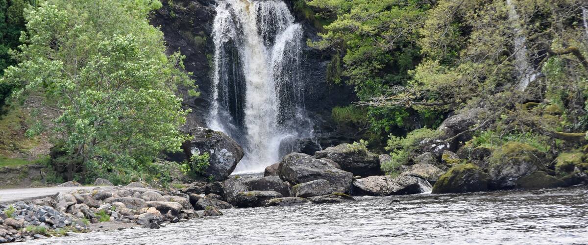 A waterfall cascading over rocks surrounded by lush greenery.