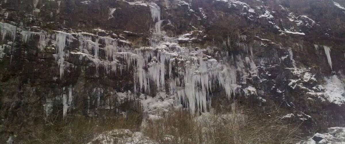A rocky cliff with icicles hanging from it.