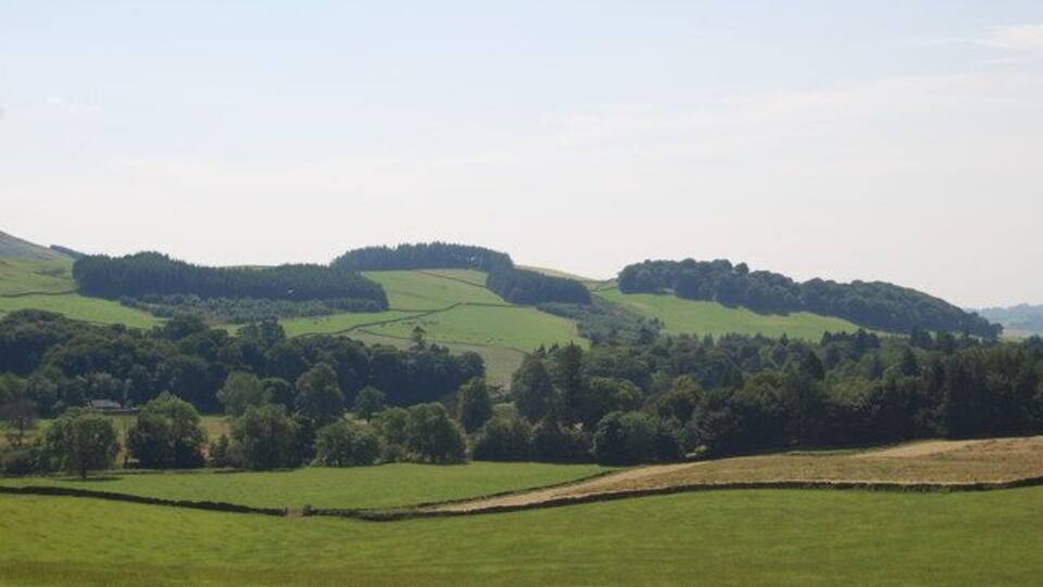 Rolling green hills, a stone wall, and a clear sky.
