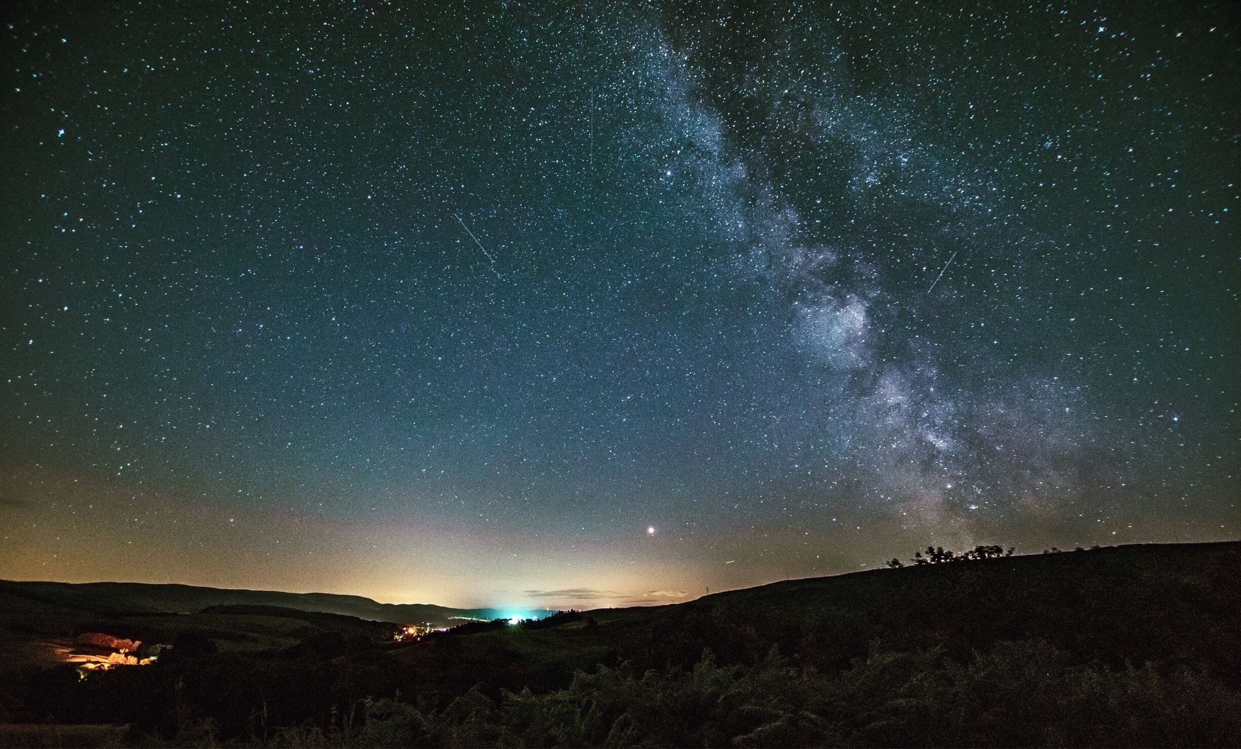 A starry night sky over a hilly landscape with a visible Milky Way.