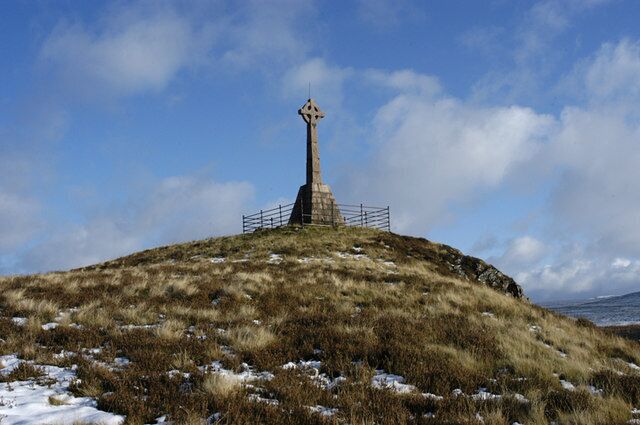 A cross-shaped monument on a grassy hill with a clear sky.