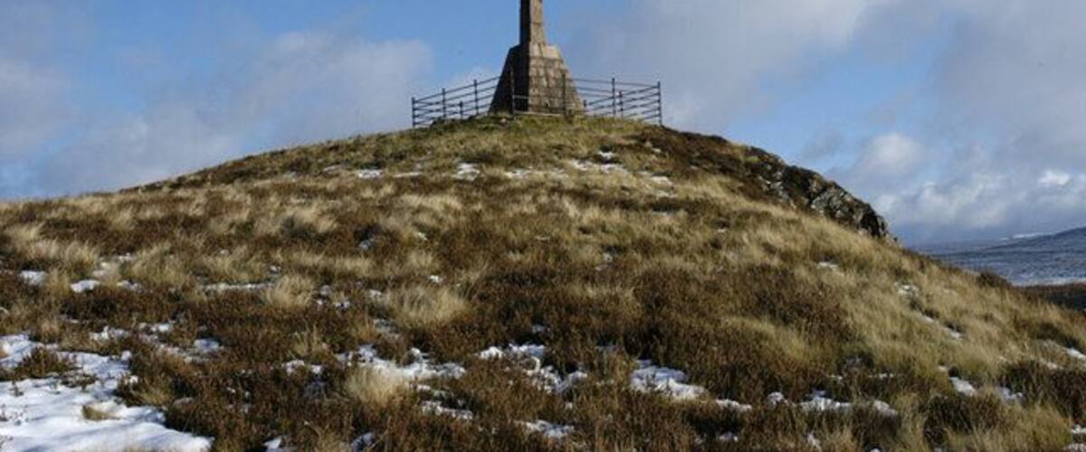 A cross-shaped monument on a grassy hill with a clear sky.