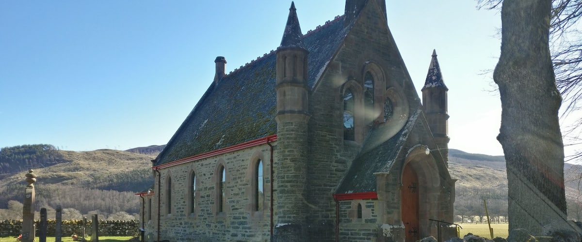 A stone church with a steeply pitched roof and a bell tower.