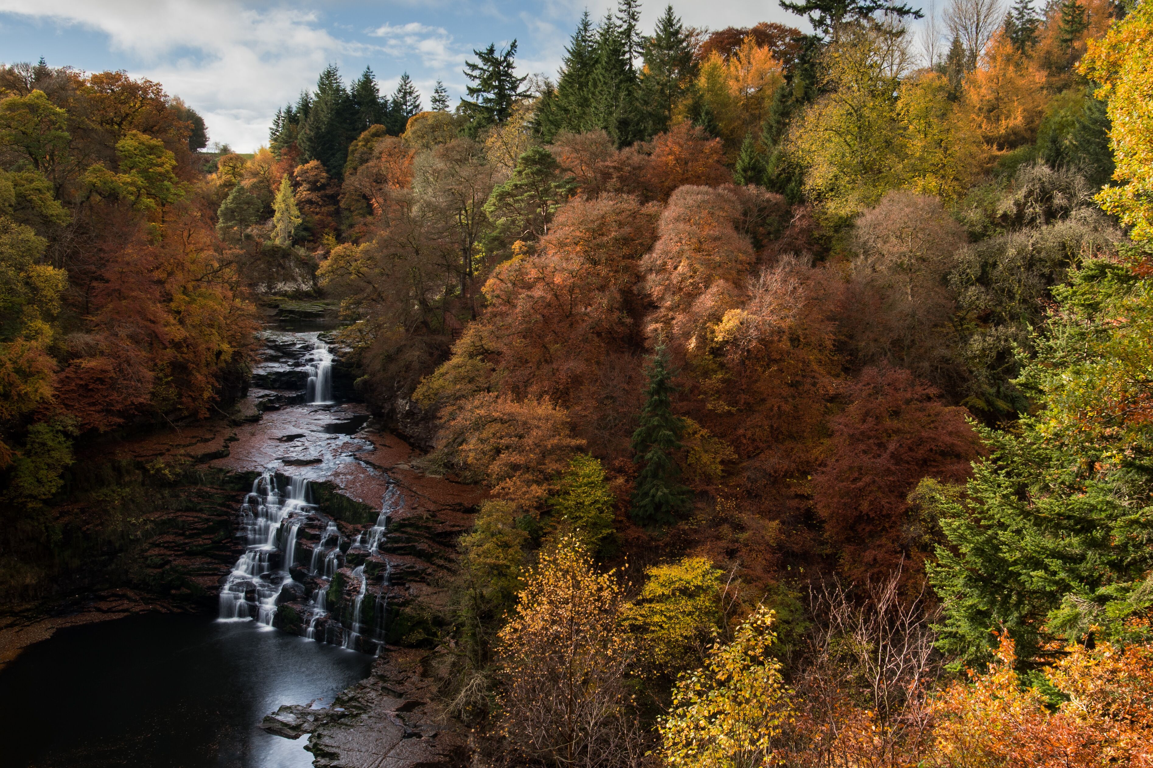 A waterfall cascading through a forest with autumn foliage.