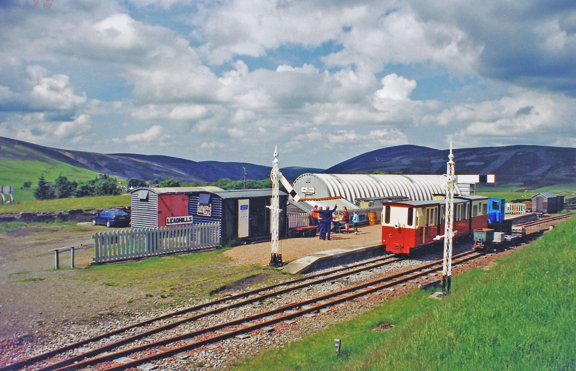 A train station with a red and white building, a blue train, and a white fence.