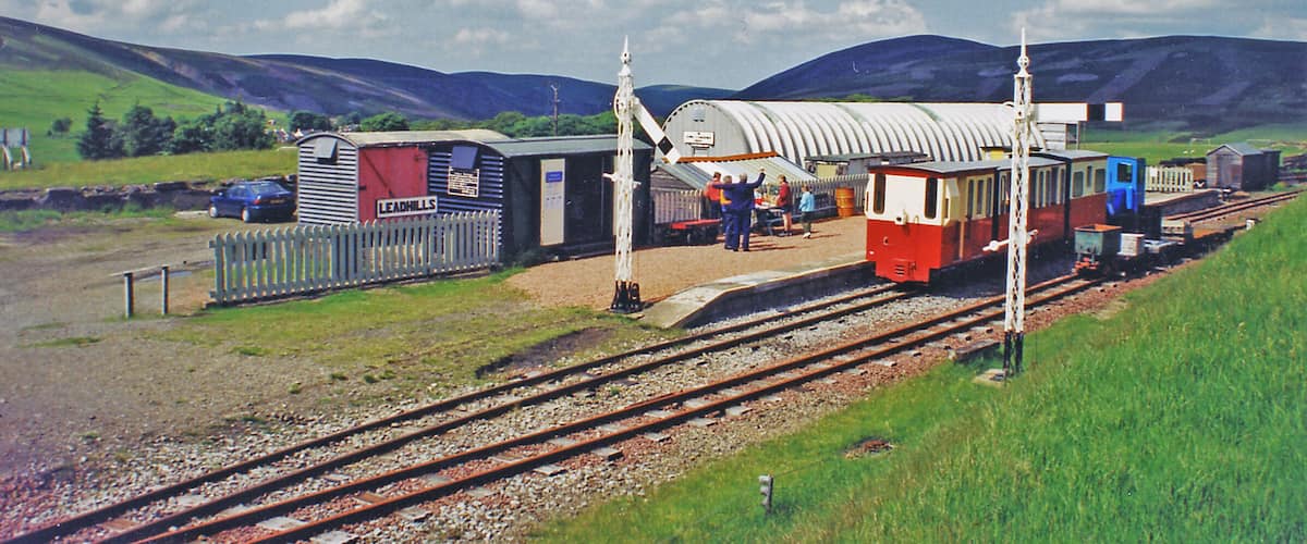 A train station with a red and white building, a blue train, and a white fence.