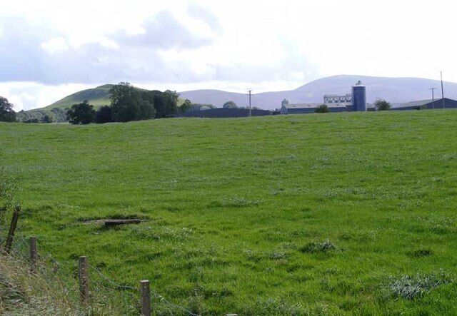 A green field with a fence, a hill, and a distant building.