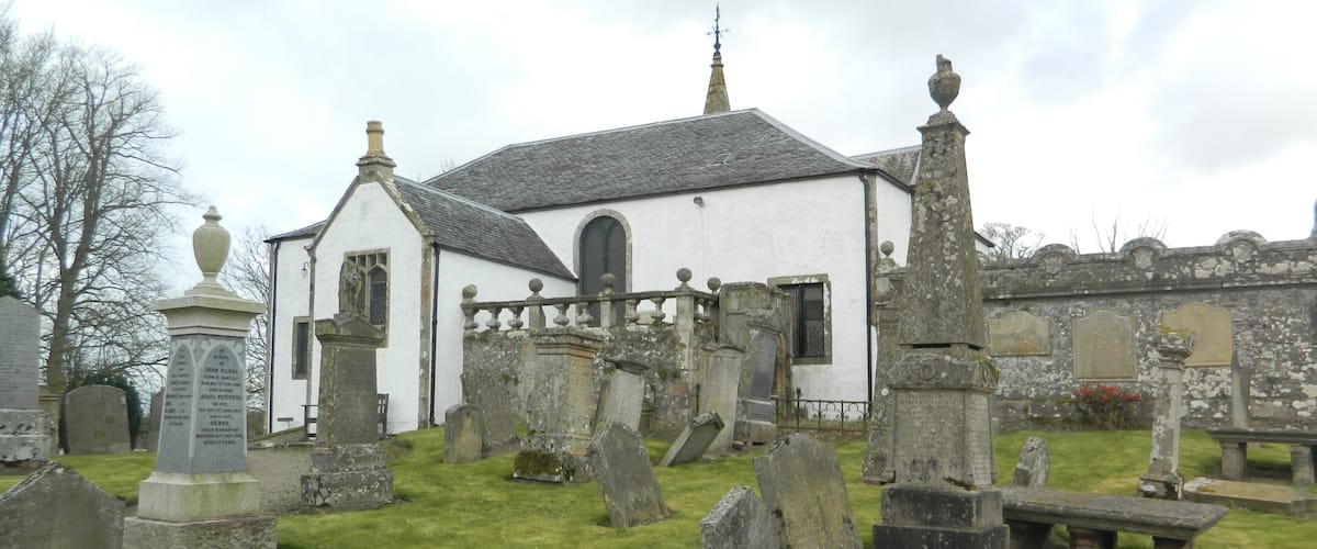 A white church with a stone fence and gravestones in the foreground.