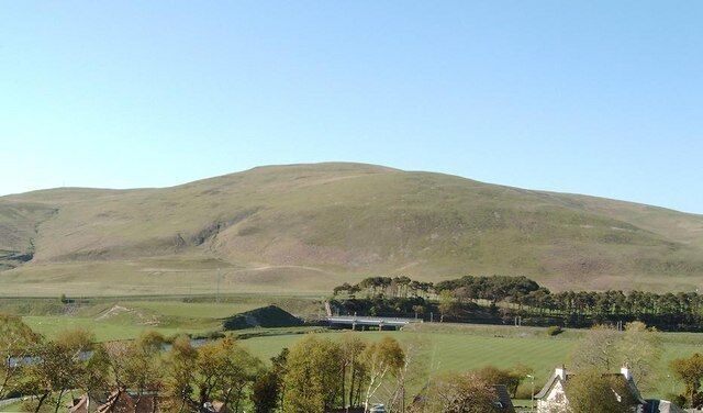 A rolling green hill, a clear blue sky, and a distant building.