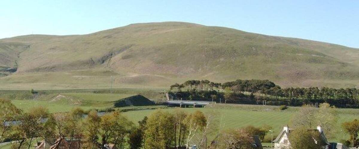 A rolling green hill, a clear blue sky, and a distant building.