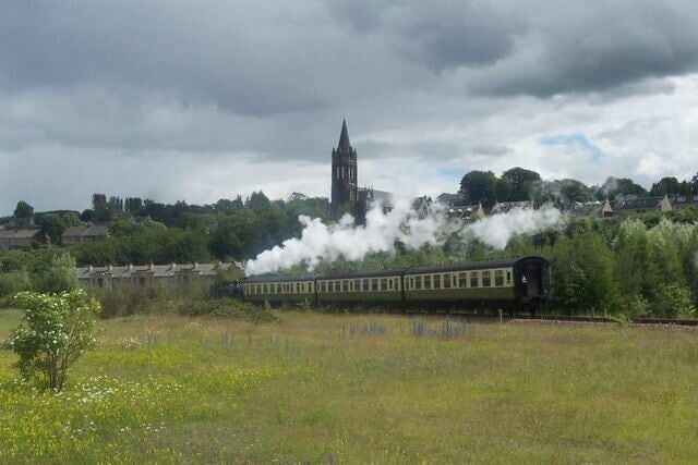 A steam train in a rural area with a church steeple in the background.