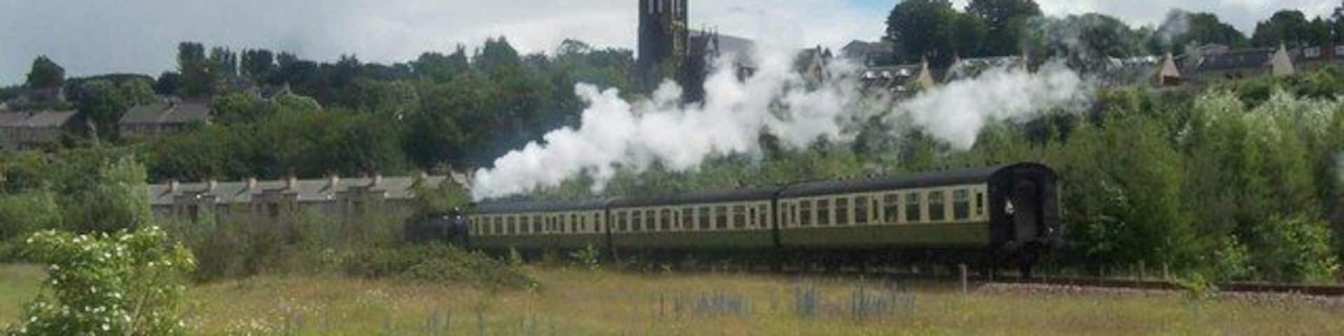 A steam train in a rural area with a church steeple in the background.