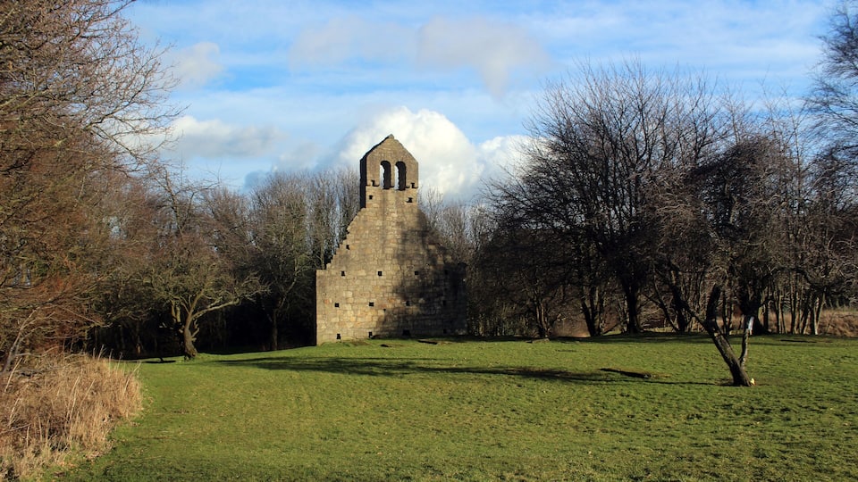 A stone tower with arched windows in a grassy field surrounded by trees.