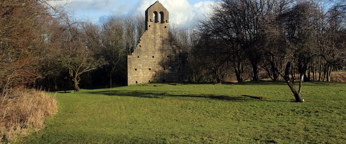 A stone tower with arched windows in a grassy field surrounded by trees.