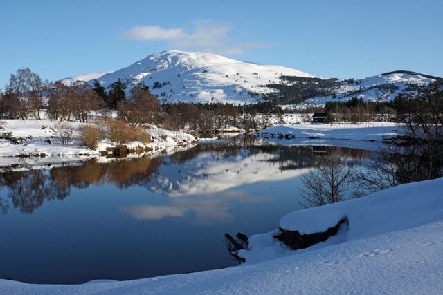 A snow-covered landscape with a mountain, a lake, and a snowbank.