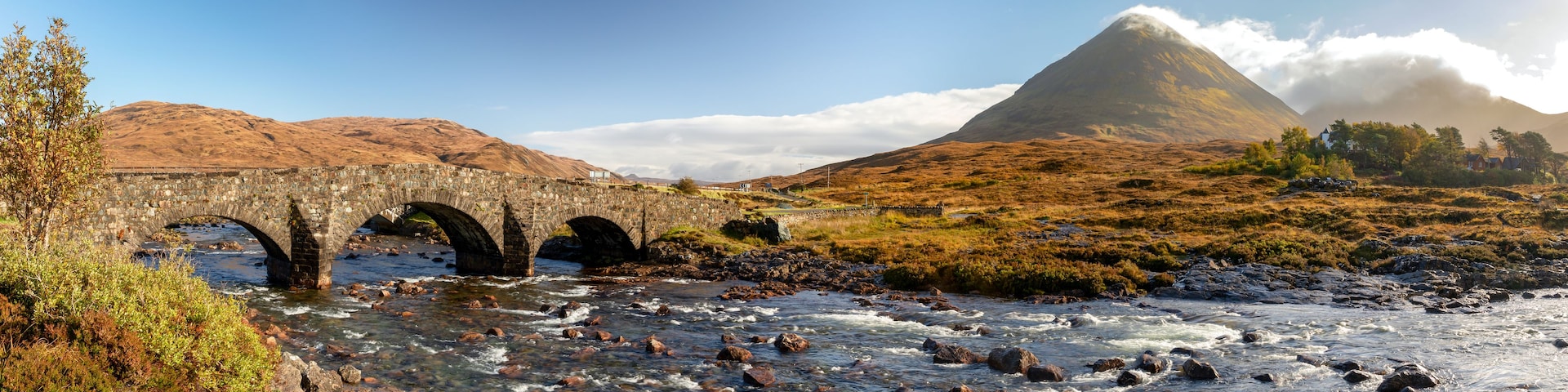 Un puente de piedra sobre un río, una montaña y un cielo despejado.