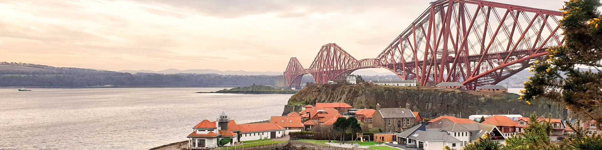 A coastal town with a prominent red bridge, houses with red roofs, and a rocky shoreline.