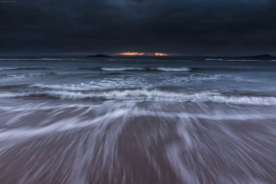 A beach with waves and a stormy sky.
