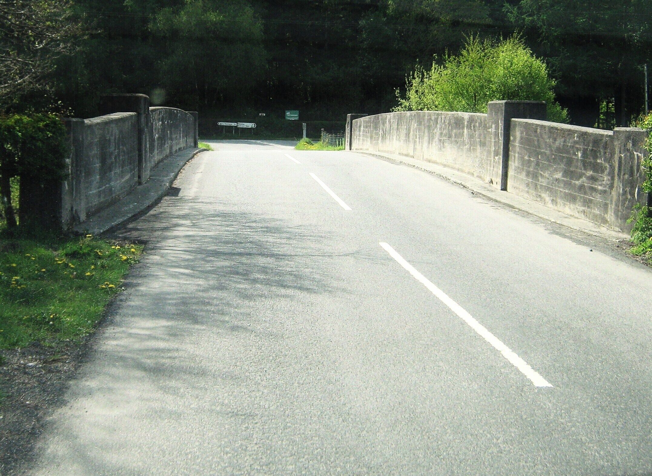 A two-lane road with a concrete bridge over a forested area.