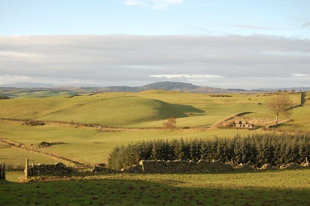 Rolling green hills, a stone wall, and a distant building.