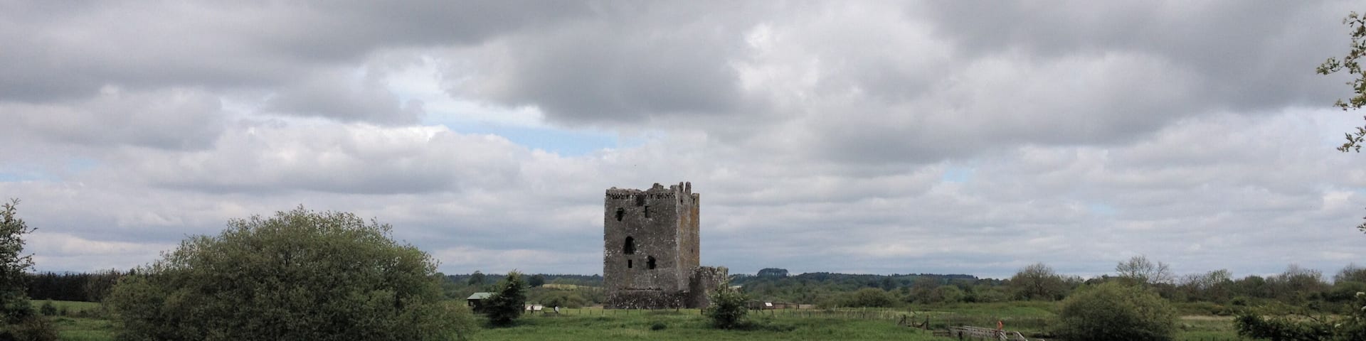 A historic stone tower by a calm river surrounded by lush greenery.