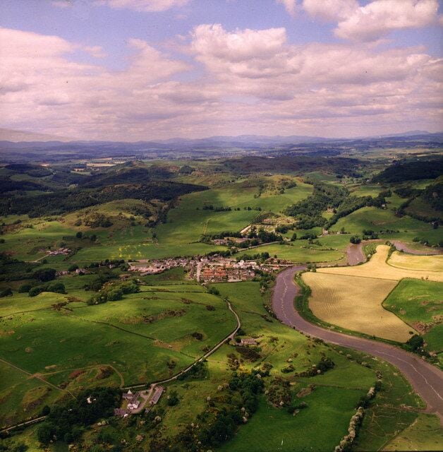 Paisaje rural con colinas ondulantes, un camino serpenteante y edificios dispersos.