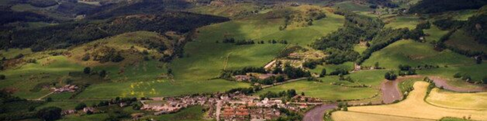 Paisaje rural con colinas ondulantes, un camino serpenteante y edificios dispersos.