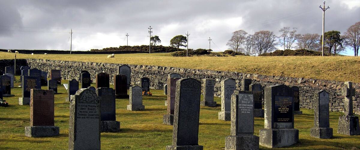 A cemetery with numerous headstones and a stone wall in the background.