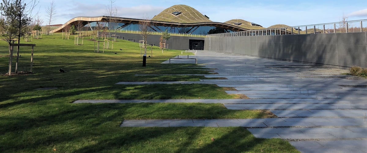 A modern building with a unique curved roof, surrounded by a well-maintained grassy area and a paved walkway.