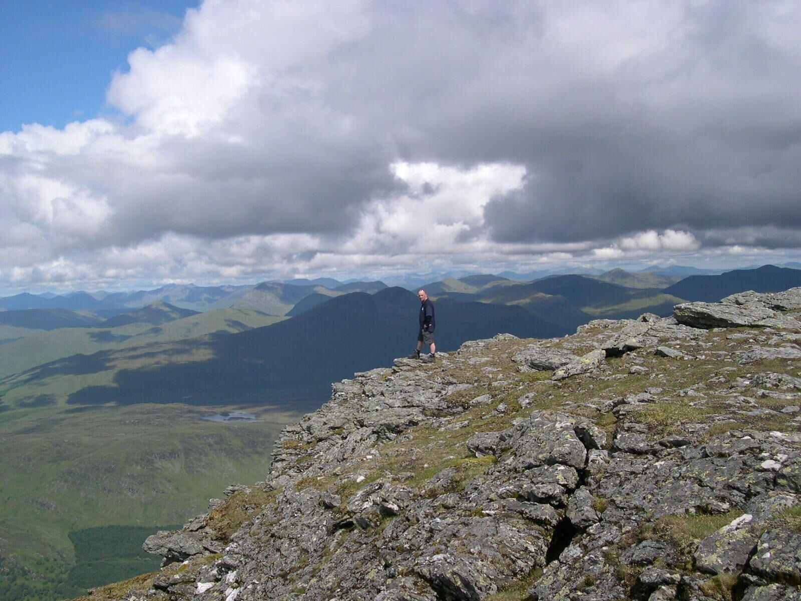 A person standing on a rocky mountain peak with a vast landscape of mountains and valleys in the background.
