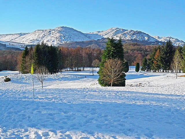 A snowy landscape with a mountain in the background and a few trees in the foreground.