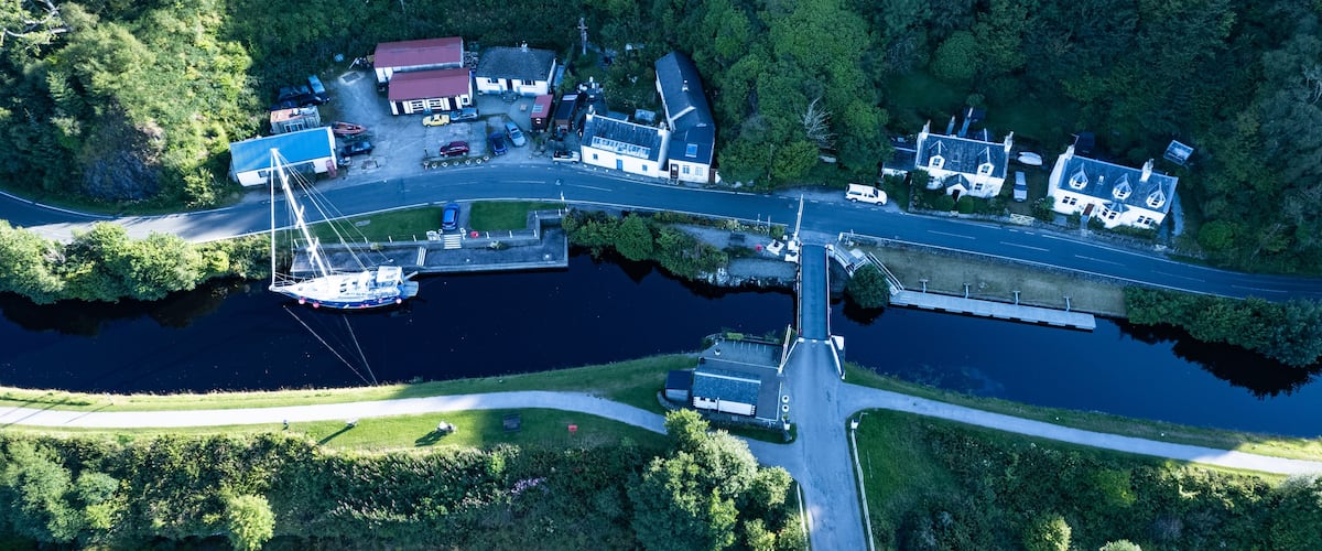 An aerial view of a riverside town with a bridge, boats, and buildings.