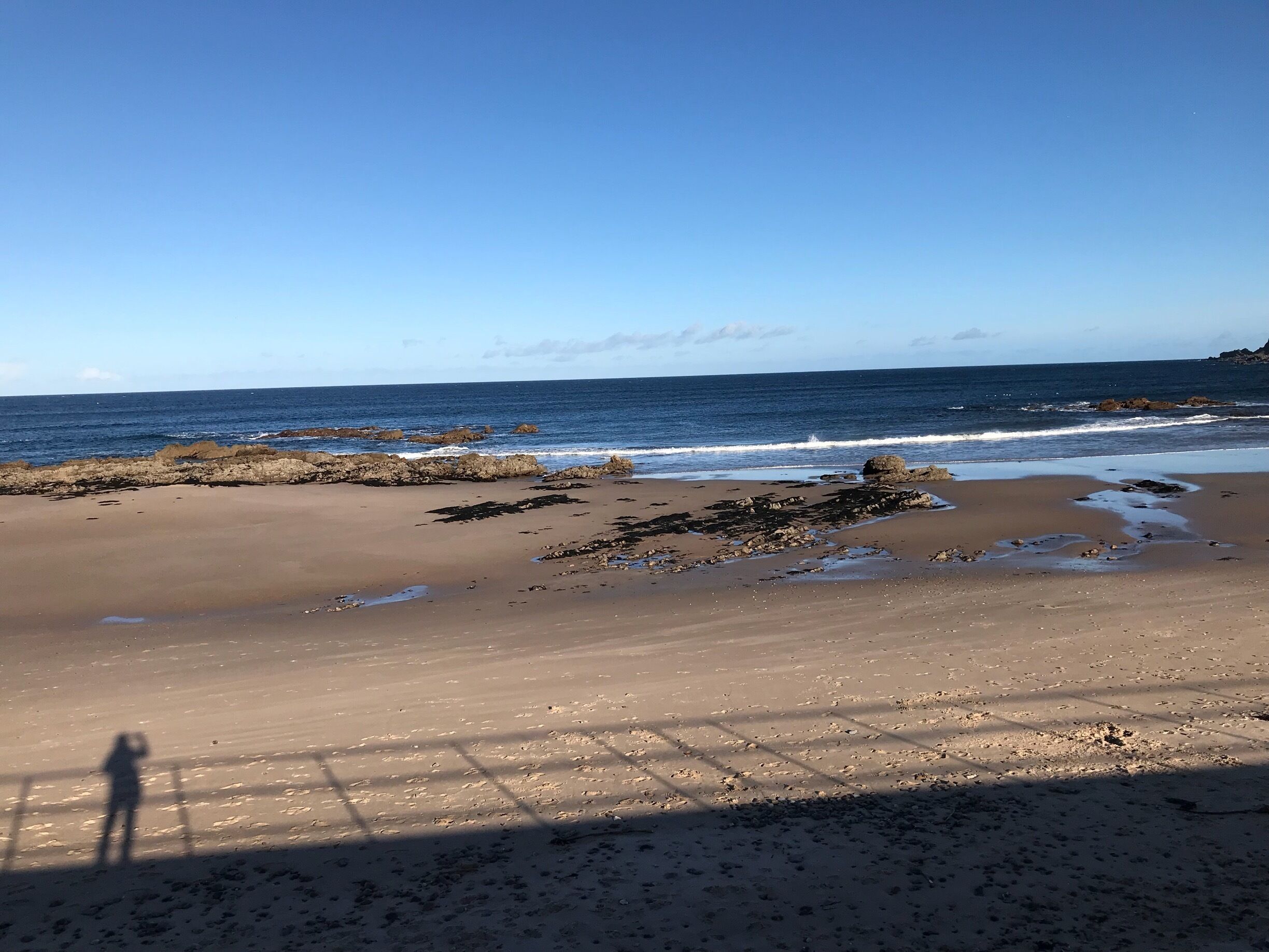 A sandy beach with scattered rocks and waves crashing onto the shore.