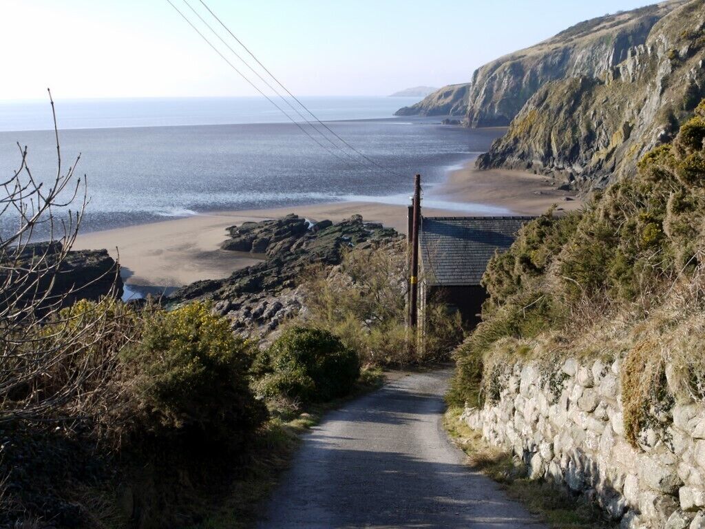 A coastal road leading to a beach with rocky cliffs and a stone wall.