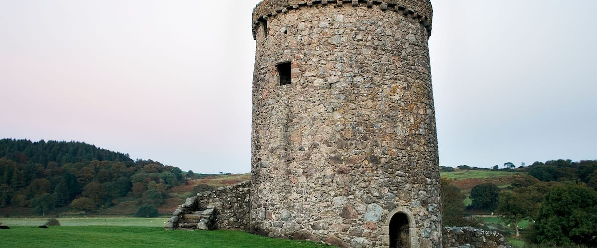 A stone tower with a circular base, a small arched entrance, and a flat roof with a crenellated top.