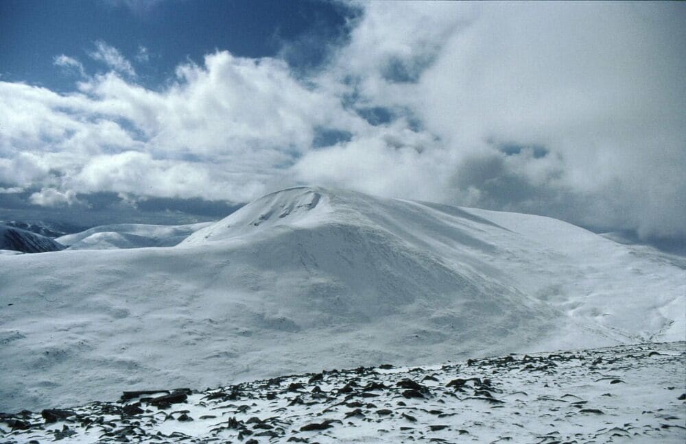 Un sommet de montagne enneigé, avec un ciel dégagé et quelques nuages.