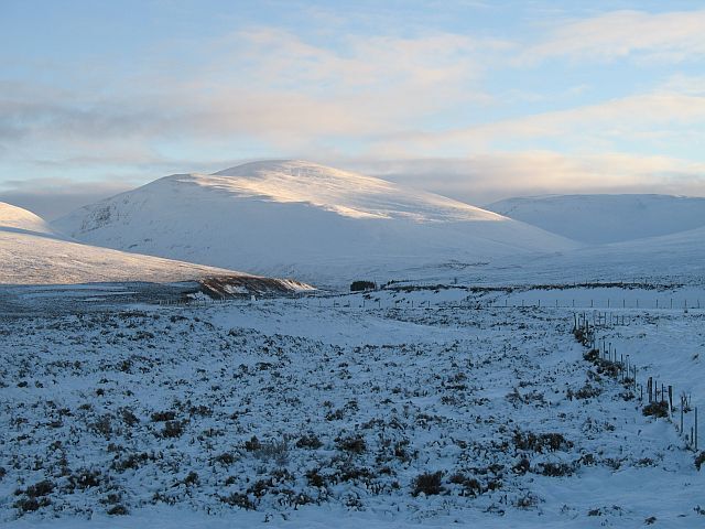A snowy landscape with a mountain in the background and a fence in the foreground.