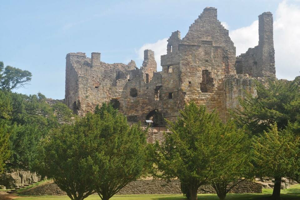 A historic stone castle with multiple towers and ruins, surrounded by green trees.