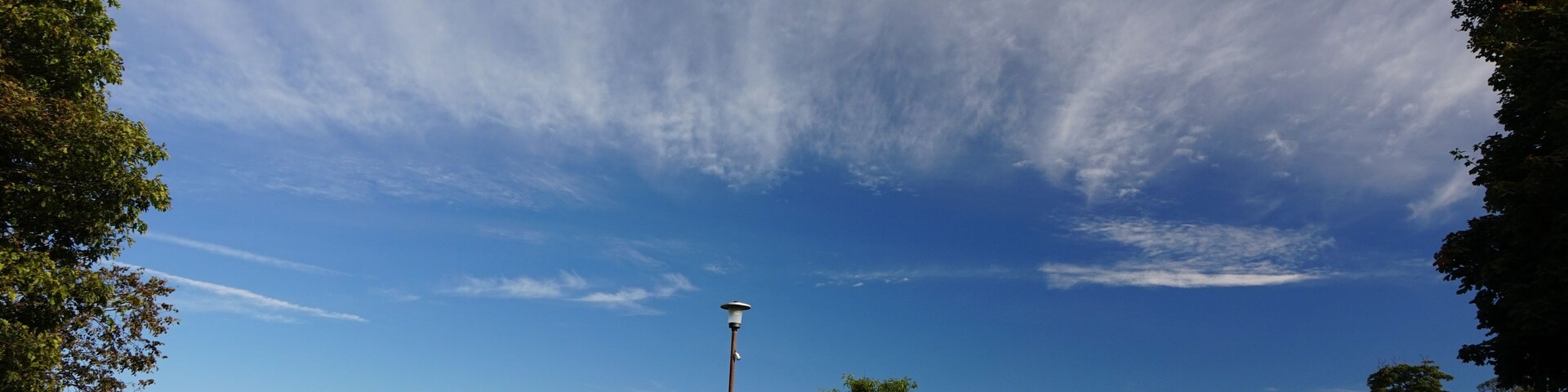 Un parque con cielo azul despejado, césped verde, una farola y una estructura de ladrillo.